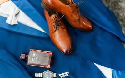 Une élégante composition à plat représentant un costume bleu, des chaussures en cuir marron, une montre-bracelet et un parfum pour le jour spécial du marié.